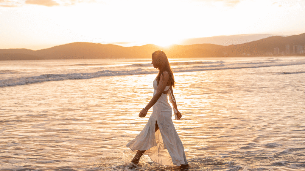 Woman walking along the ocean at sunrise, symbolizing spiritual growth and building capacity for her calling.”