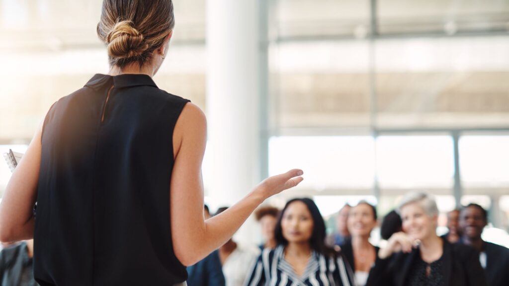 Woman speaking to an audience in a room, sharing an inspiring message about storytelling and impact.